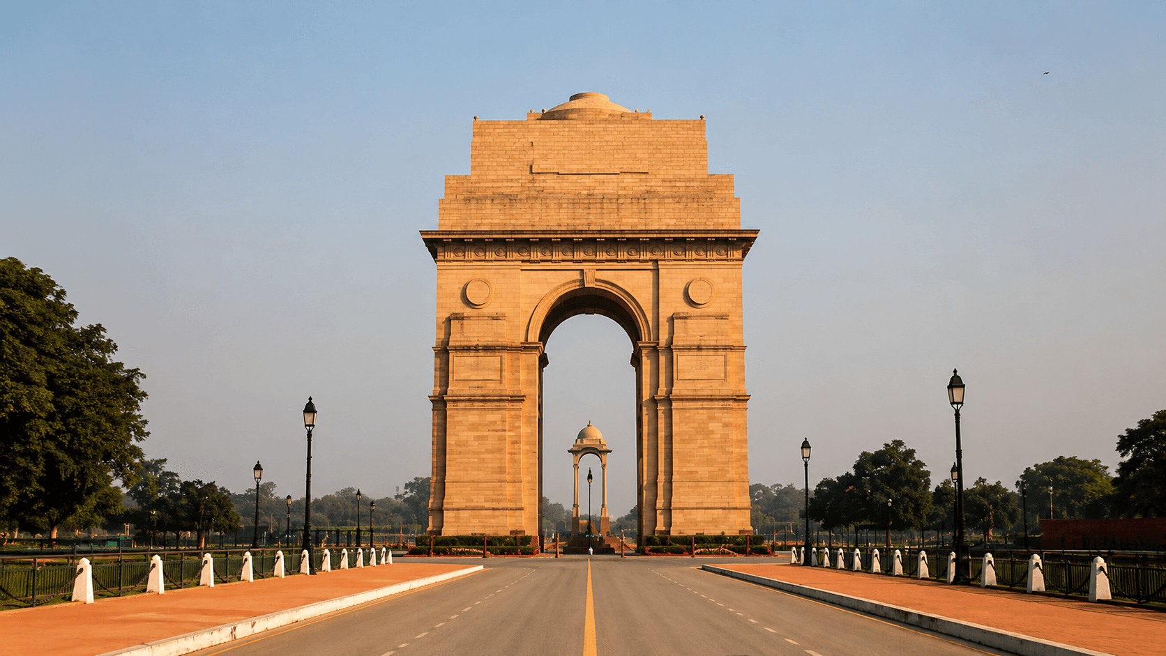 A monumental archway framing a tree-lined New Delhi boulevard at golden hour.